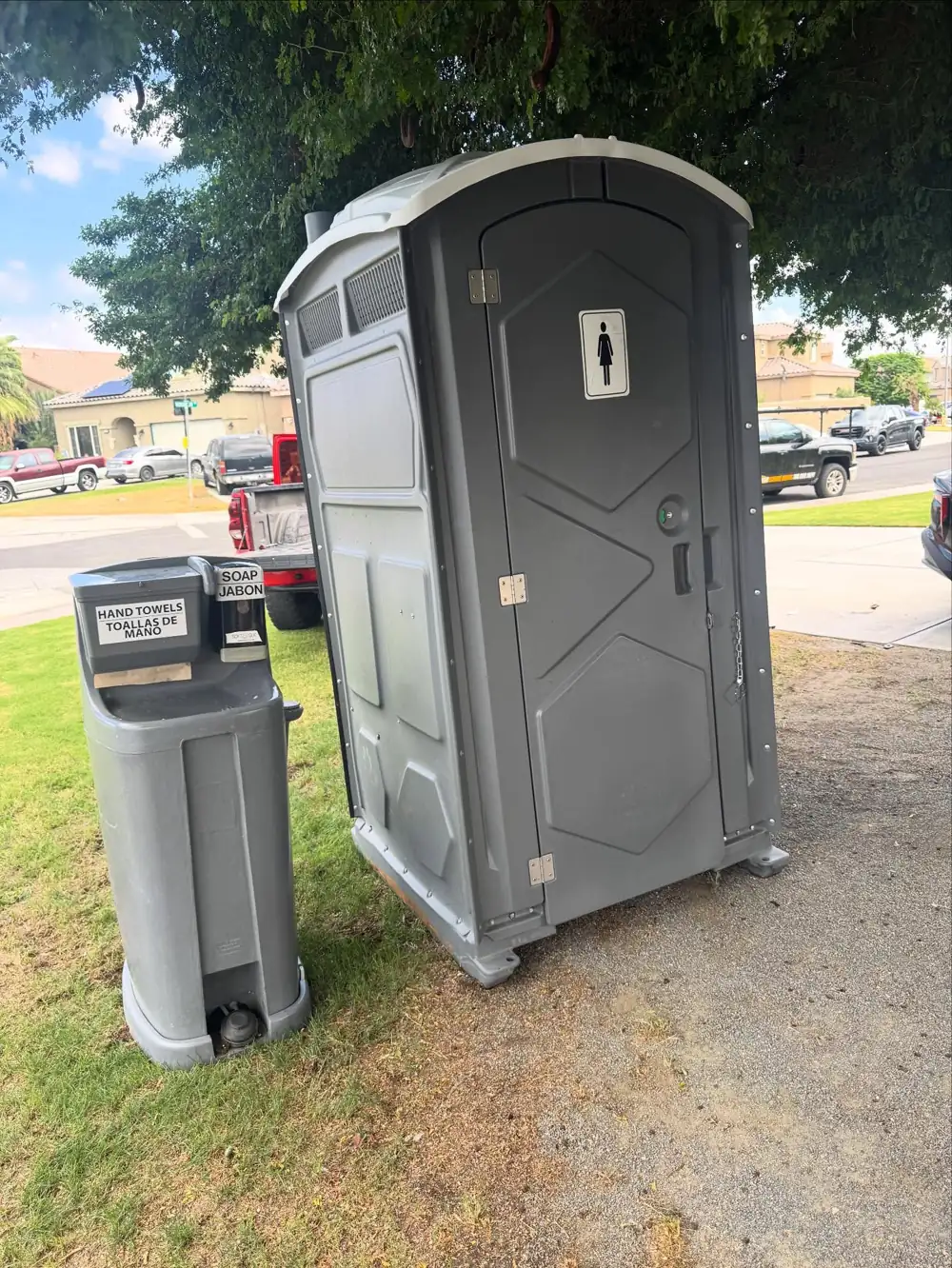 Porta potty and hand-wash station on a shaded lawn