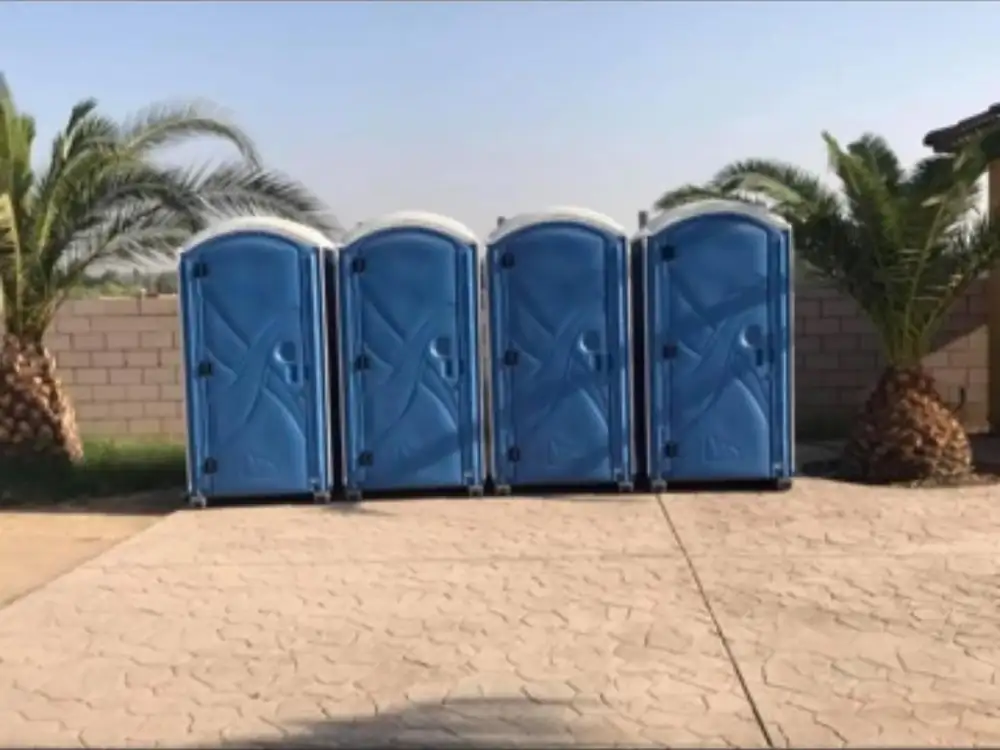 Four blue porta potties lined up on a paved driveway for an event